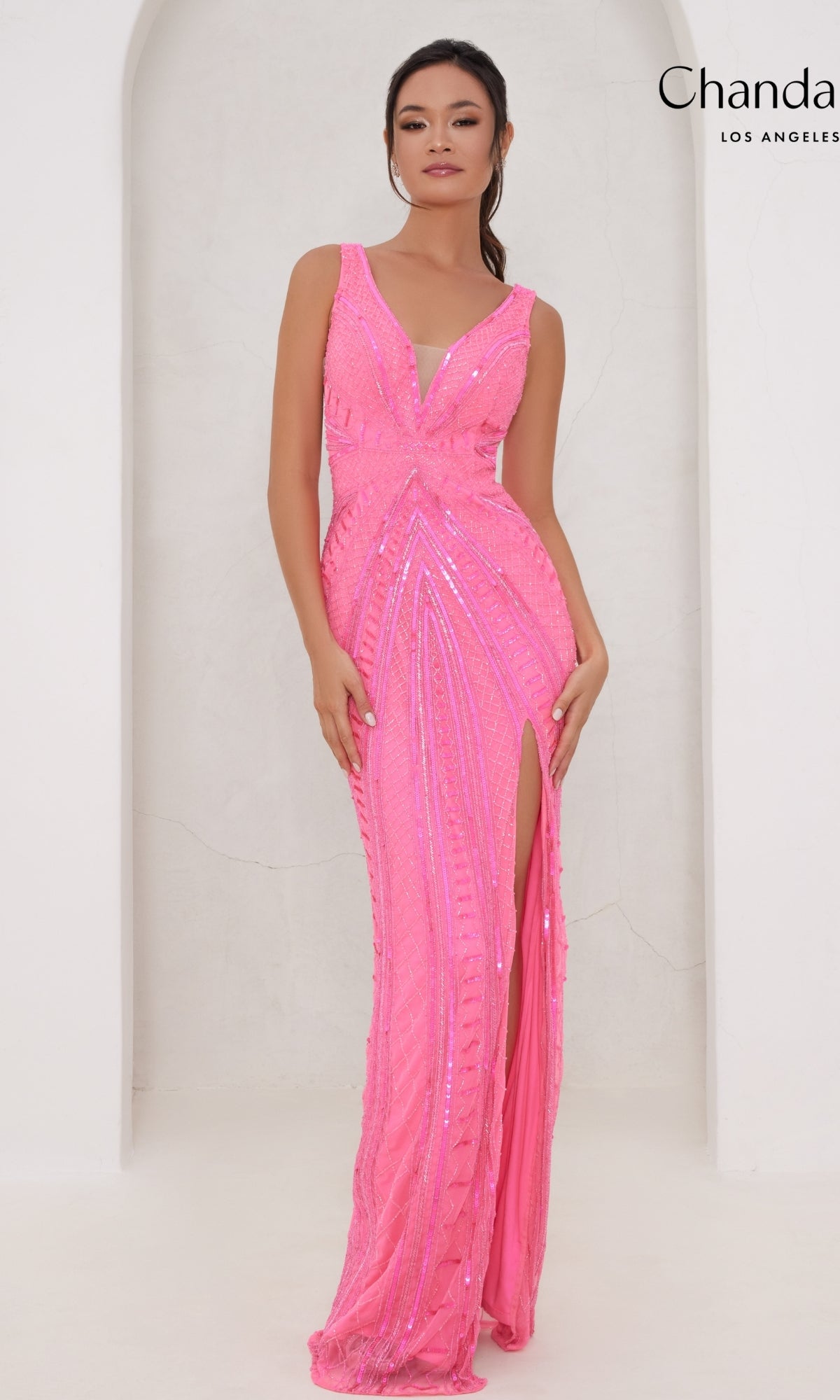 A woman wearing the Long Prom Dress 30091 by Chandalier—a sleeveless, floor-length pink sequin gown with a high slit and open back—stands against a white background.